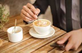 A person is sitting at a table with a cup of coffee and a small container of sugar.