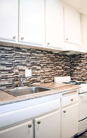 A kitchen with white cabinets and a stone backsplash.
