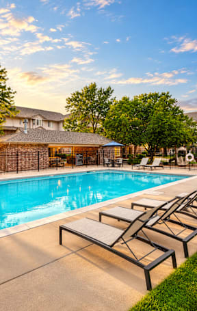 A pool with sun loungers and a house in the background.