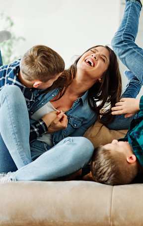 A family of three is lying on a beige couch.