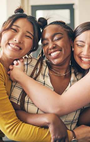 Three women hugging each other in a living room.