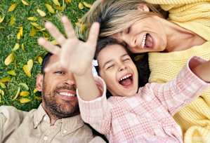 A family of three is lying on the grass with their hands in the air.