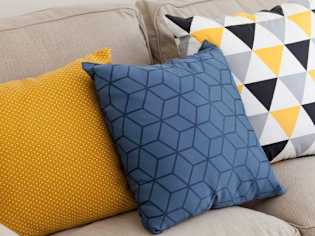 Three pillows on a beige couch with different patterns.