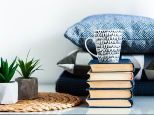 a stack of books on a table with plants and pillows