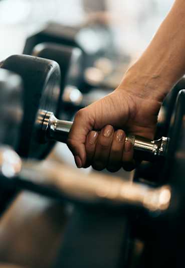 A person's hand is holding a dumbbell in a gym.