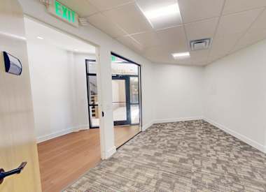 A room with a carpeted floor and a green exit sign on the wall.