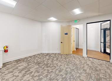 A room with a carpeted floor, a white wall, a wooden door, and a white cabinet with a red object on top.