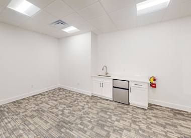 A white room with a grey carpet and a fridge.