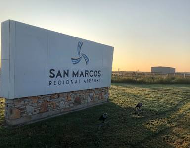 A sign for San Marcos Regional Airport with a bird on the grass.