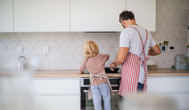 a man and a little girl standing in a kitchen cooking on a stove