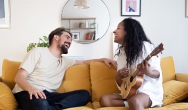 a couple sitting on a yellow couch playing a guitar