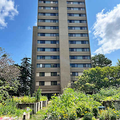 a tall concrete building with many windows is surrounded by greenery.