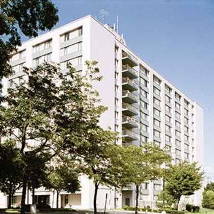a tall white building with balconies and trees in front.