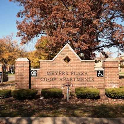 a sign for meyers plaza co-op apartments stands in front of a tree.