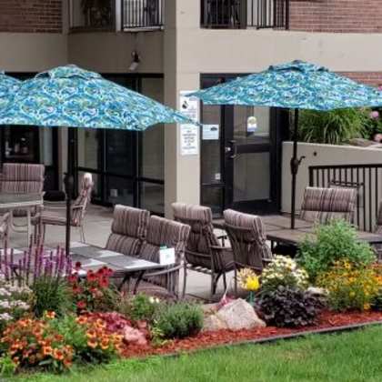 a patio with chairs and umbrellas is surrounded by a flower garden.