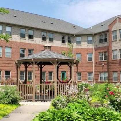 a gazebo is surrounded by flowers in a courtyard between two red brick buildings.