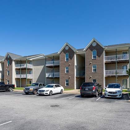 a parking lot in front of a multi-story apartment building with cars parked.