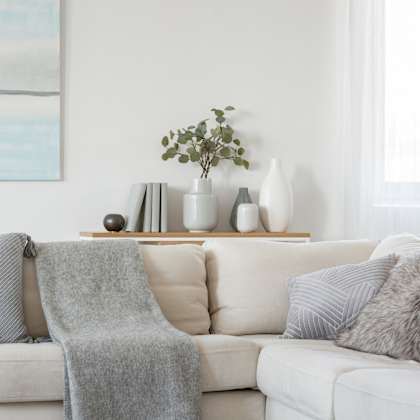a white couch with grey pillows and a grey blanket.