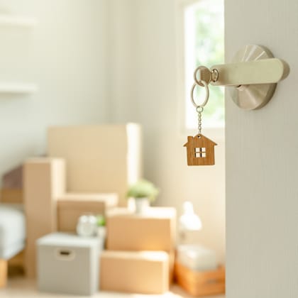 a key hanging from a door handle with boxes and a plant in the background.