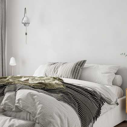 a bed with a white comforter and a green striped blanket.
