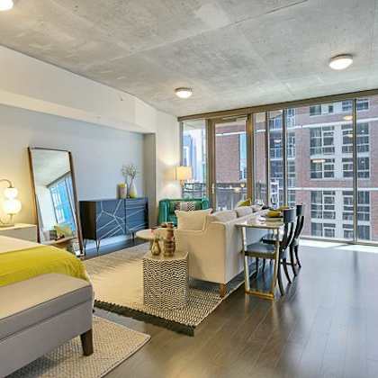 a bright studio-style apartment here at victory place with floor-to-ceiling windows, dark wood flooring, a modern kitchen, cozy living area, and a sleeping space with green accent bedding and stylish decor.