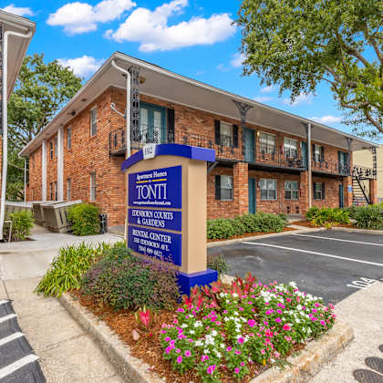 a sign for the tonni gardens apartments is in front of a brick building.