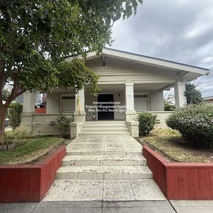 a white building with a porch and a tree in front.
