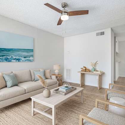 a living room with a beige couch, a coffee table, and a painting of a beach scene on the wall.