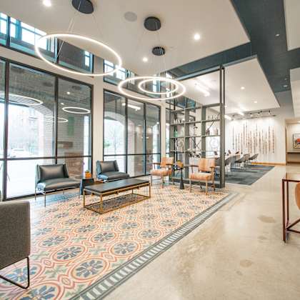 a modern waiting room with a patterned carpet and a mix of grey and orange seating.