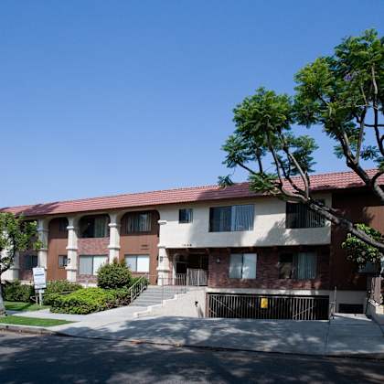 a brown apartment building with a red roof and a tree in front.
