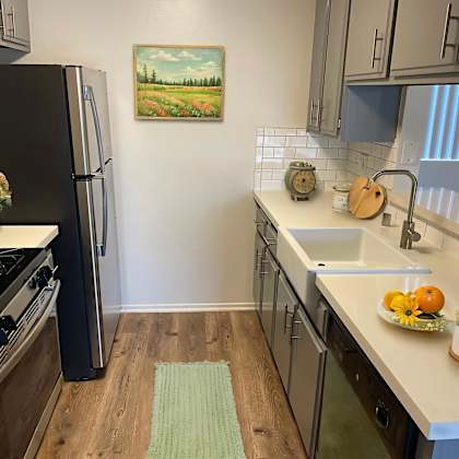 a kitchen with a black refrigerator, wooden floors, and a painting of a field on the wall.