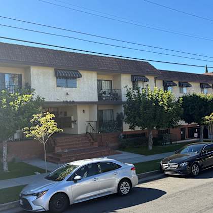 a silver car is parked in front of a white building with a black car parked behind it.