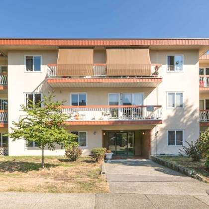 a large white apartment building with balconies and a driveway in front.