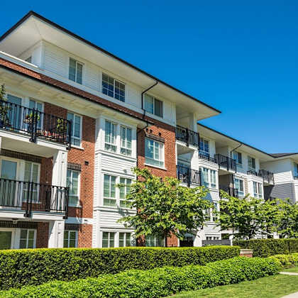 a row of apartment buildings with balconies and green hedges in front.