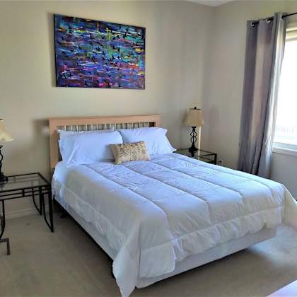 a bed with a white comforter and pillows is in a room with a painting on the wall.