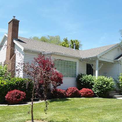 a house with a grey roof and a red tree in front.