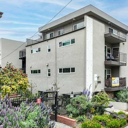 a grey building with a balcony and a small garden in front.