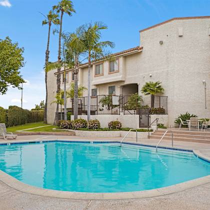 a swimming pool in front of a building with palm trees.