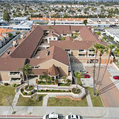 a large building with a brown roof is surrounded by a parking lot and palm trees.