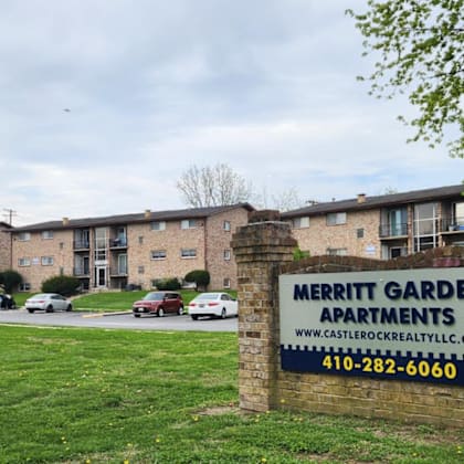 a brick sign that says merritt garden apartments stands in front of apartment buildings.