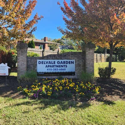 a sign for delvale garden apartments is surrounded by flowers and trees.