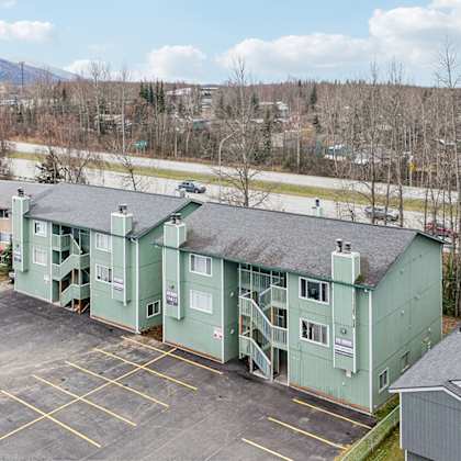 a parking lot in front of a green building with a mountain in the background.