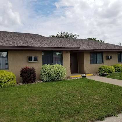 a house with a brown roof and beige walls with bushes in front.