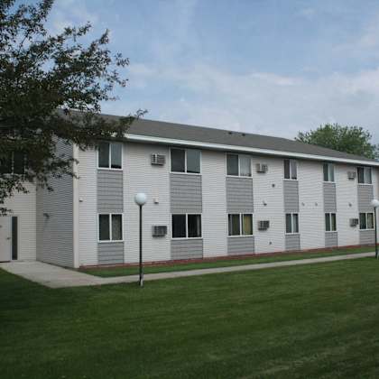 a white building with a grey roof and a green lawn in front.