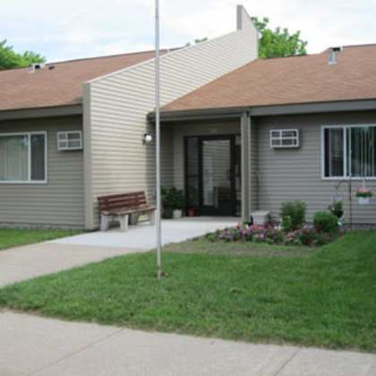 a grey building with a brown bench in front.