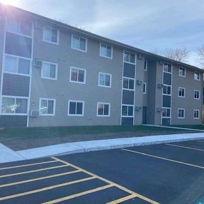 a sunny day at the apartment complex with a parking lot in front.