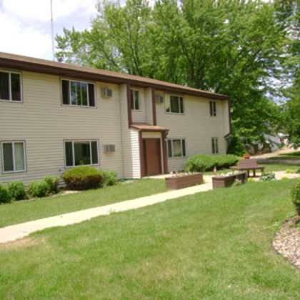 a beige two-story apartment building with a brown door and windows.