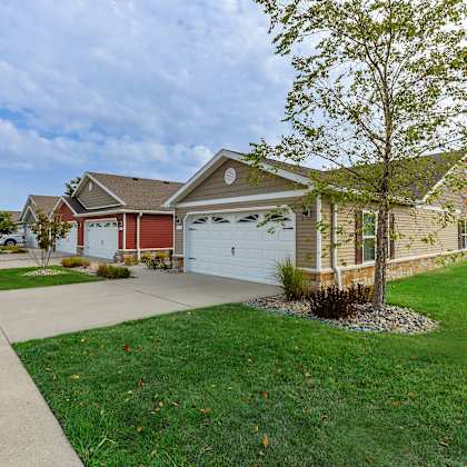 a house with a red garage door is surrounded by a well-kept lawn and a sidewalk.