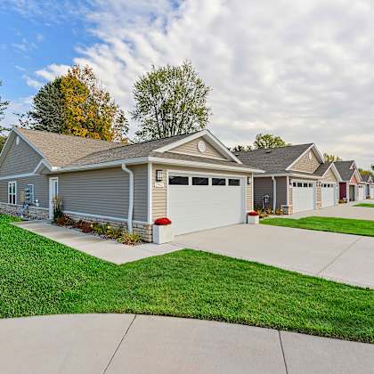 a house with a grey garage door is surrounded by a green lawn.