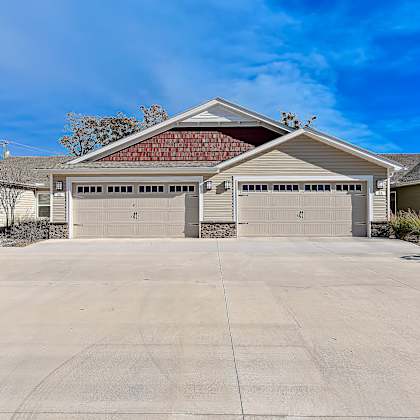a two-car garage with a red roof is surrounded by a concrete driveway and other houses.